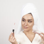 Young woman in a bathrobe looking at a lipstick . High quality photo
